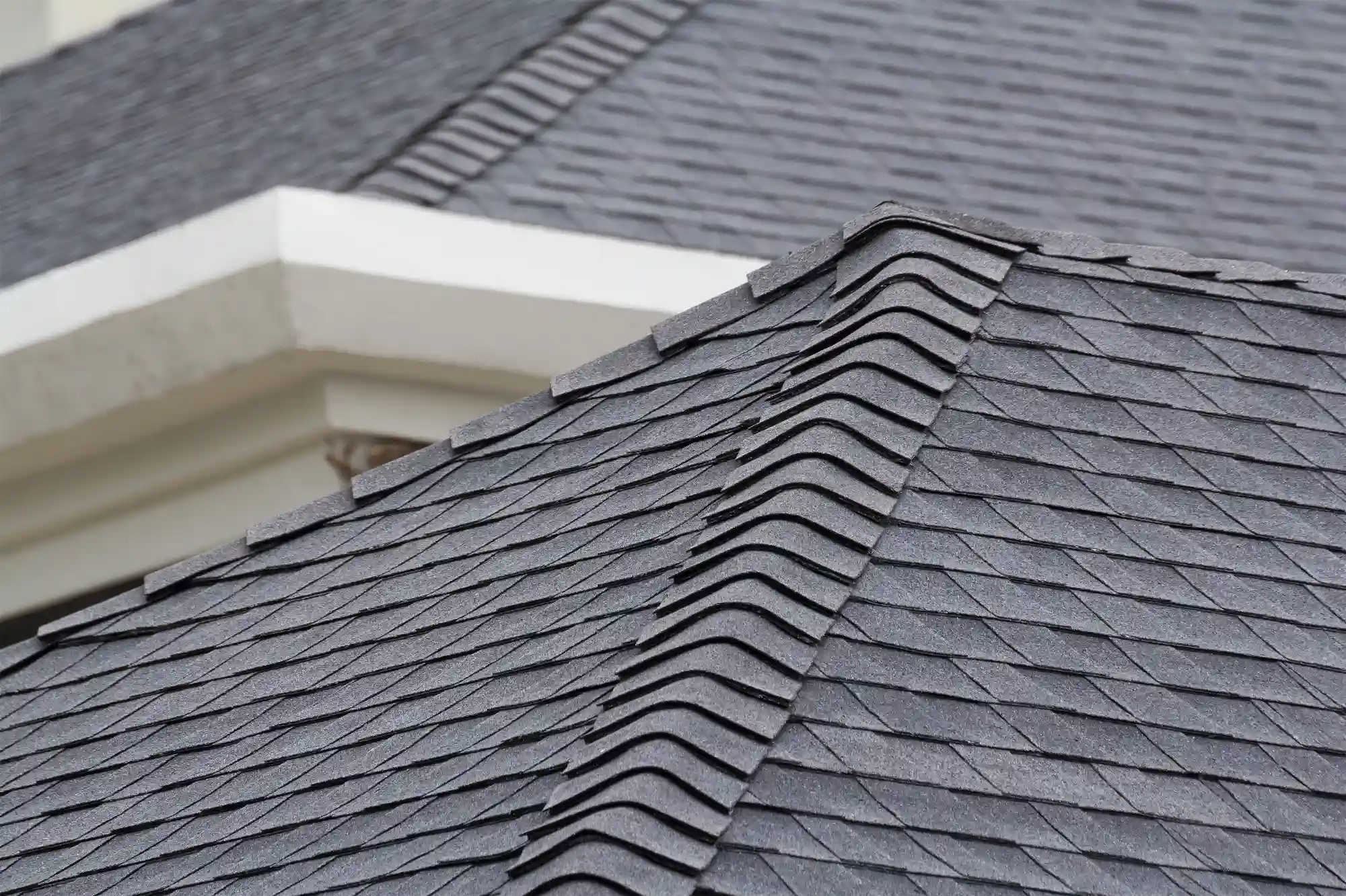 Close-up view of a house roof with dark gray asphalt shingles neatly arranged by Exterior Done Best, a trusted Twin Cities roofing company. The ridge cap shingles highlight a clean and well-maintained appearance.